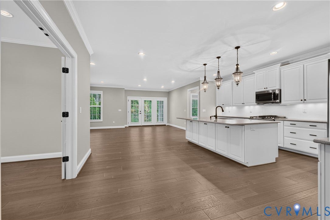 7238 Shenfield Avenue, Minutes To Short Pump, Glen Allen, VA 23059 Open-concept kitchen and living area featuring wood-finish flooring, white cabinetry, a large kitchen island with seating, pendant lighting, and double French doors to the exterior