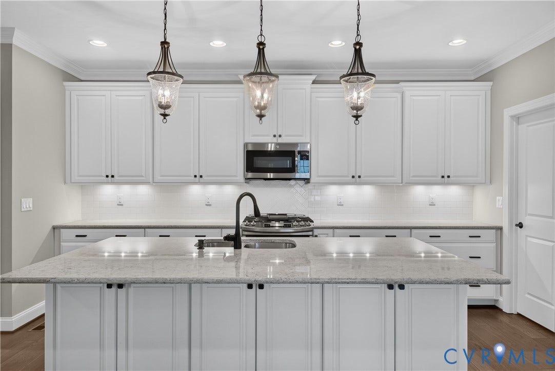 7238 Shenfield Avenue, Minutes To Short Pump, Glen Allen, VA 23059 Modern kitchen featuring an expansive island with a light-toned countertop, a stainless steel microwave, white shaker-style cabinetry with dark hardware, a white subway tile backsplash, and three pendant light fixtures