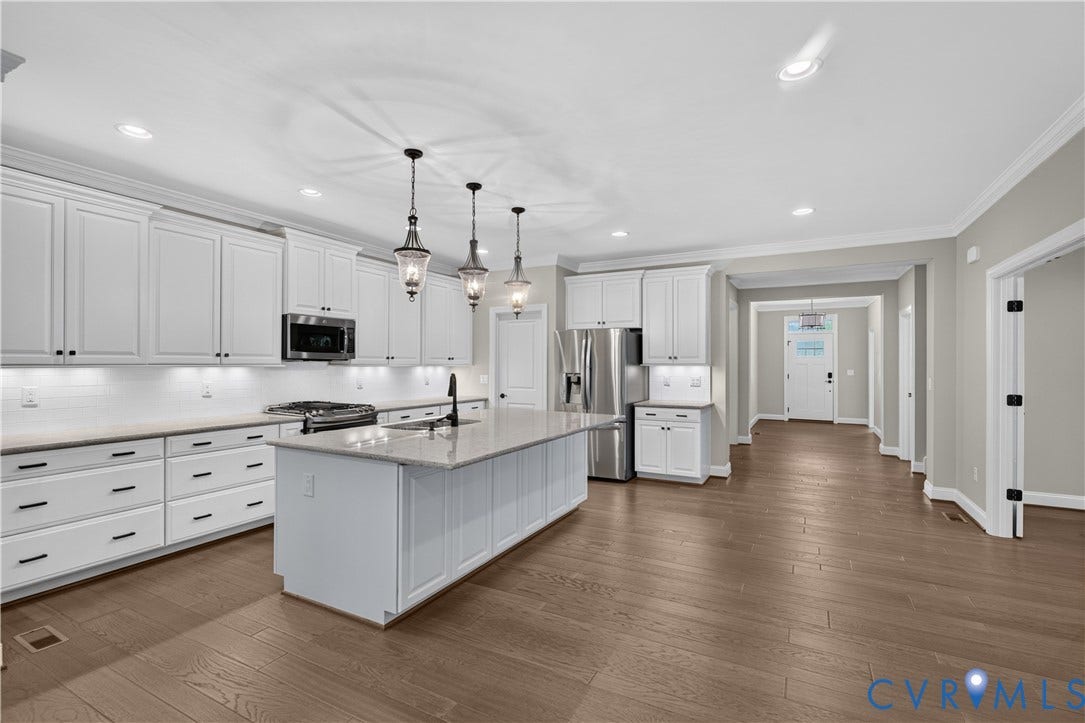 7238 Shenfield Avenue, Minutes To Short Pump, Glen Allen, VA 23059 Open-concept kitchen featuring an oversized island with a built-in sink, white shaker cabinetry, stainless steel appliances, and wood-finish flooring