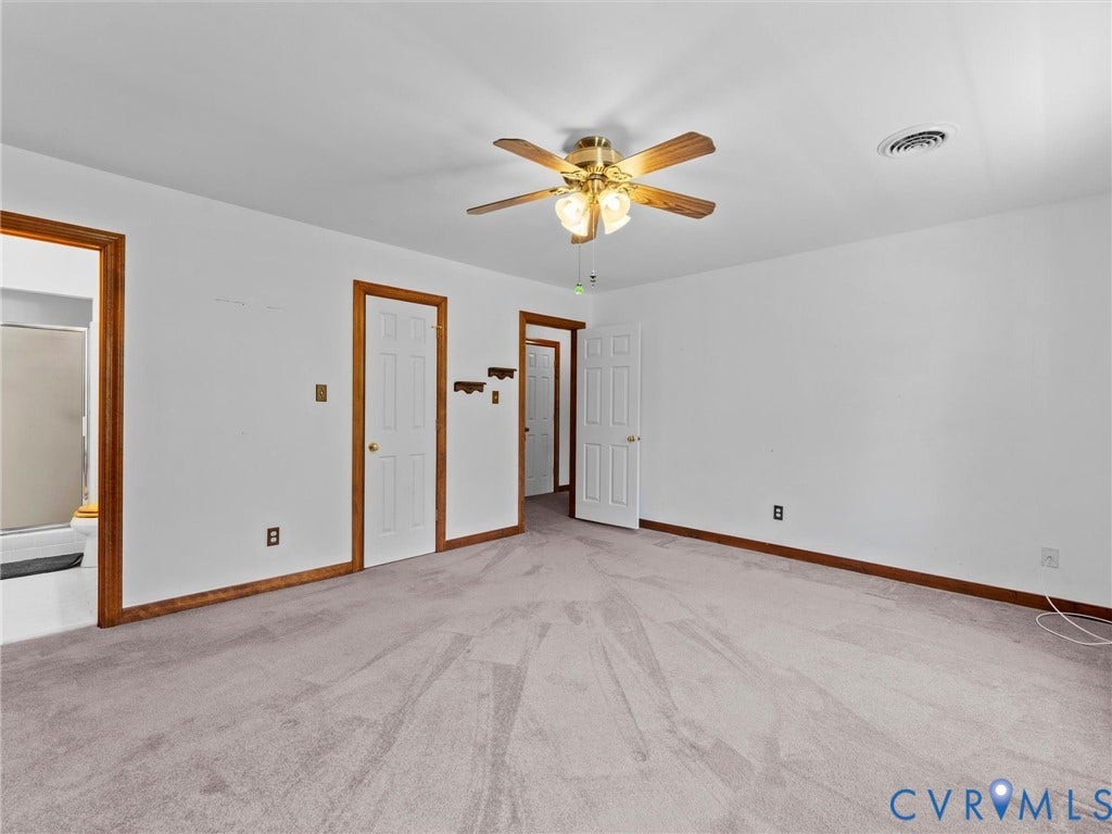 Spacious room featuring light gray carpeting, crisp white walls, and warm wood-finish trim