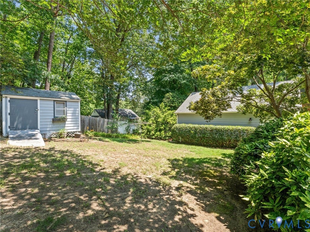 Expansive backyard featuring a storage shed with ramp access, mature trees, manicured green space, and privacy landscaping