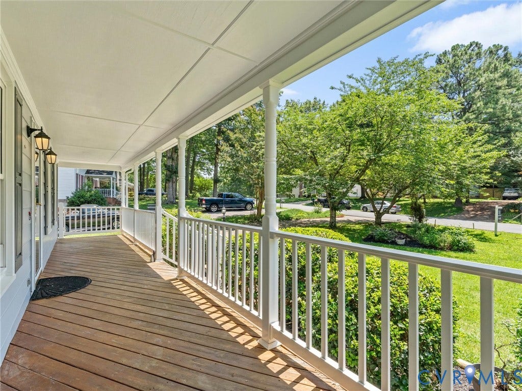 Covered front porch featuring wood-finish flooring, white railing, and decorative exterior lighting