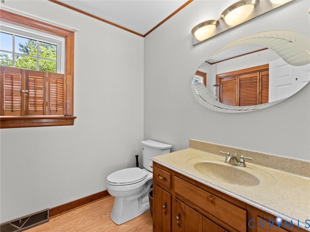 Bathroom featuring a wood-finish vanity with a built-in sink, a vanity mirror with an integrated light fixture, and wood-finish flooring