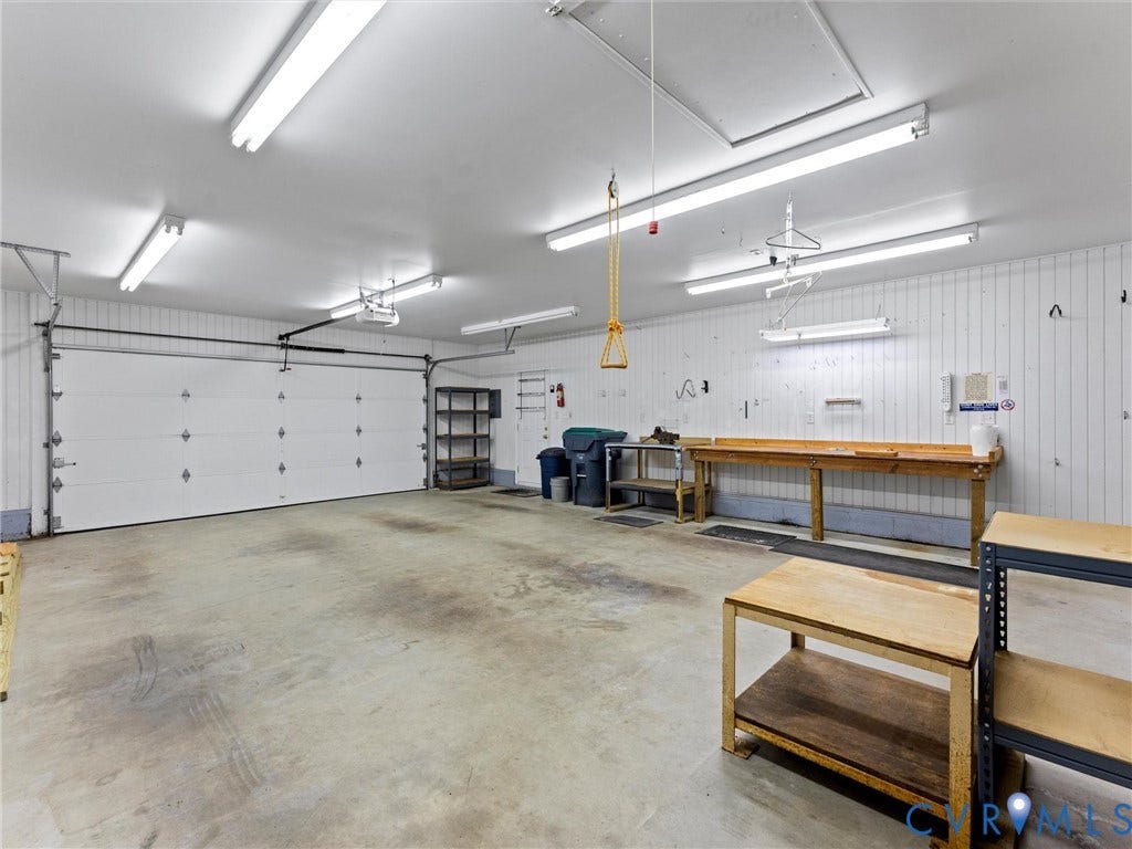Spacious interior garage featuring a concrete floor, white panel walls, multiple fluorescent light fixtures, and an overhead garage door