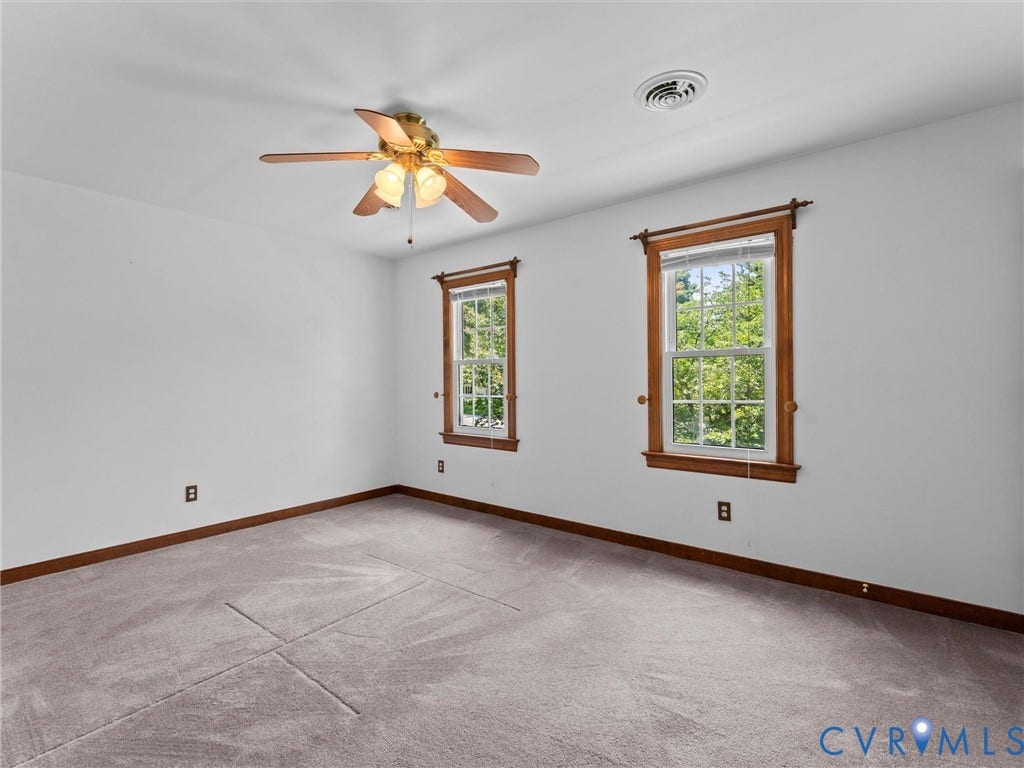 Carpeted room featuring two double-hung windows with wood-finish trim, a ceiling fan with integrated lighting, and a ceiling air vent