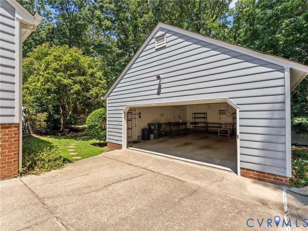 Detached garage featuring light gray horizontal siding, red brick foundation, and a concrete driveway