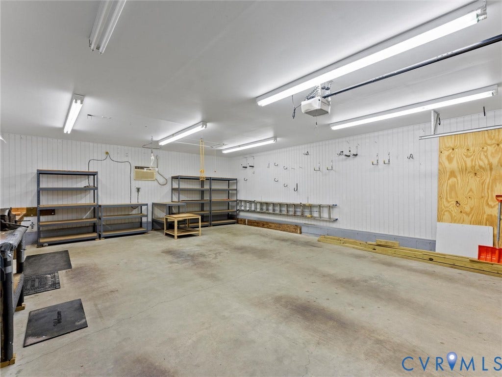 Spacious garage featuring concrete flooring, white paneled walls, and multiple fluorescent ceiling lights
