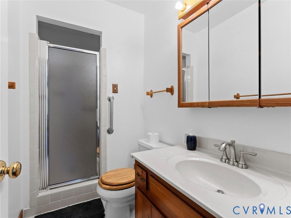 Bathroom featuring a shower with a frosted glass door, a toilet with a wood-finish seat, a vanity with a white countertop and integrated sink, a wood-frame medicine cabinet, and a chrome grab bar