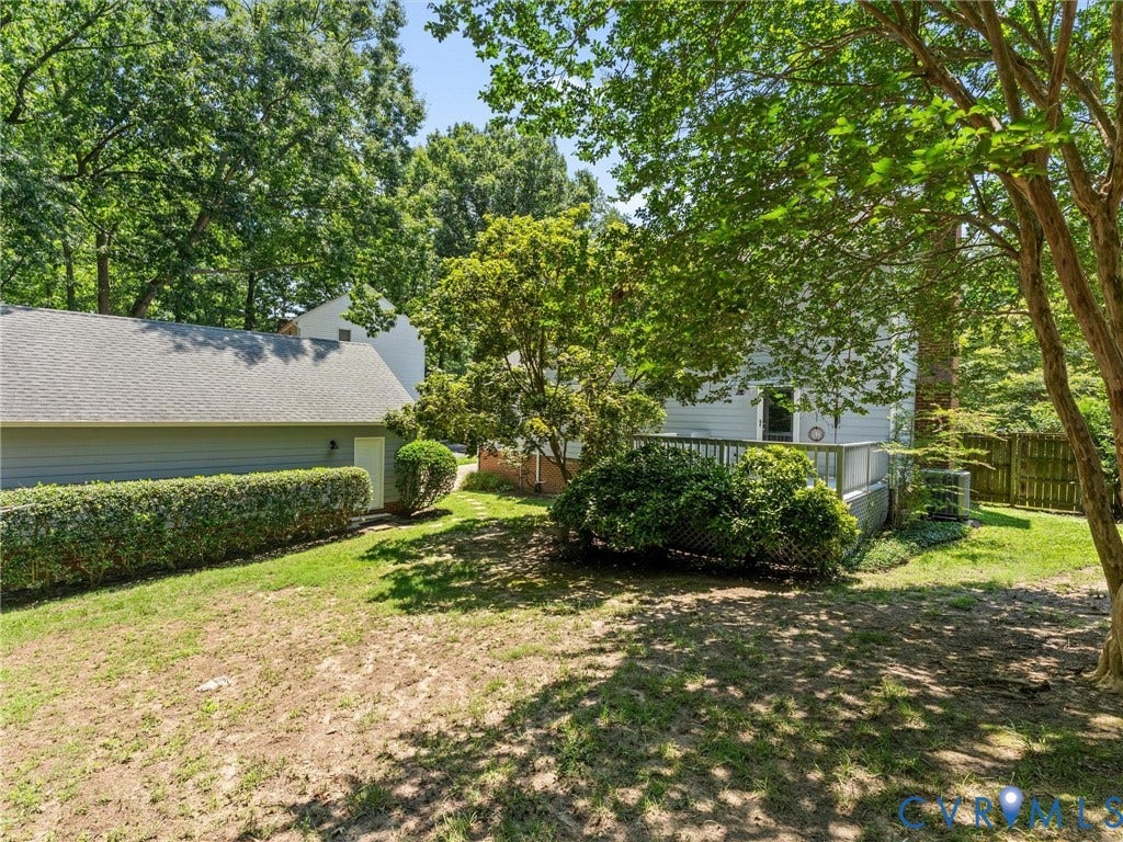 Expansive backyard featuring a wood deck, mature trees, and a low-maintenance hedge row