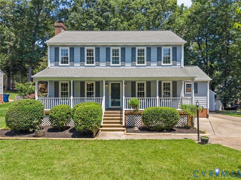 Traditional two-story home featuring a covered front porch with white railings, blue siding, and white-framed windows with dark shutters