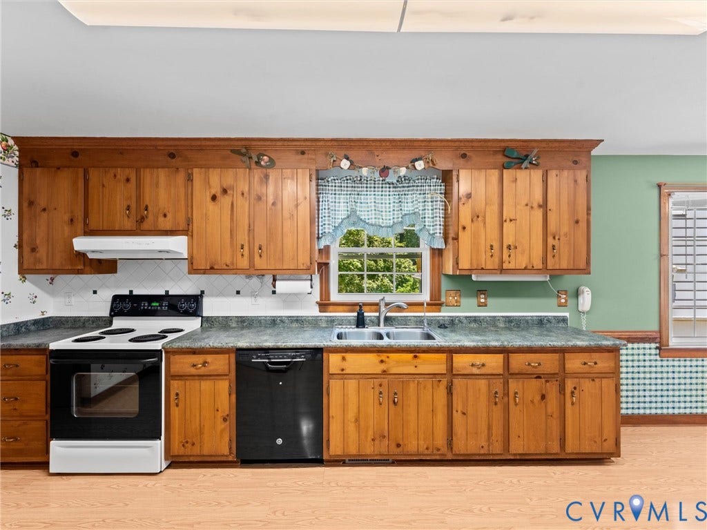 Kitchen featuring wood cabinetry, laminate countertops, a double basin stainless steel sink, tile backsplash, and wood-finish flooring