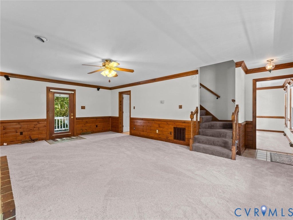 Spacious room featuring light-colored carpeting, wood paneling, and a wood-trimmed ceiling fan