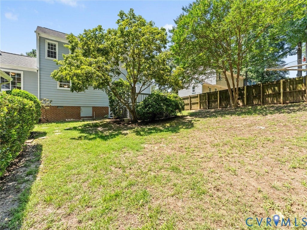 Spacious rear yard featuring a partial wood privacy fence, mature trees, and established perimeter hedges