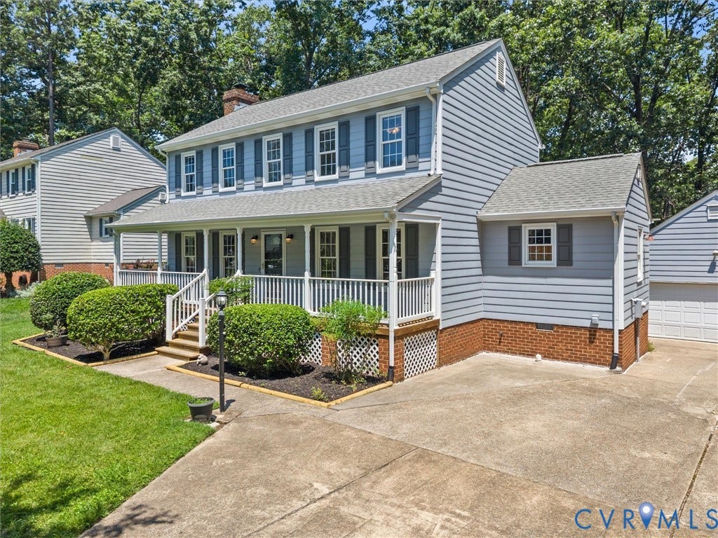 Two-story residence featuring light blue siding, a covered front porch with white railings, a concrete driveway, a two-car garage, and mature landscaping