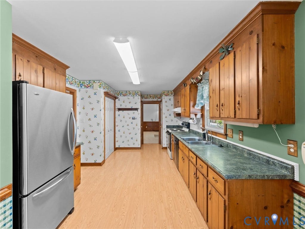 Galley kitchen featuring wood-finish flooring, wood cabinetry, stainless steel refrigerator, and green mottled countertops