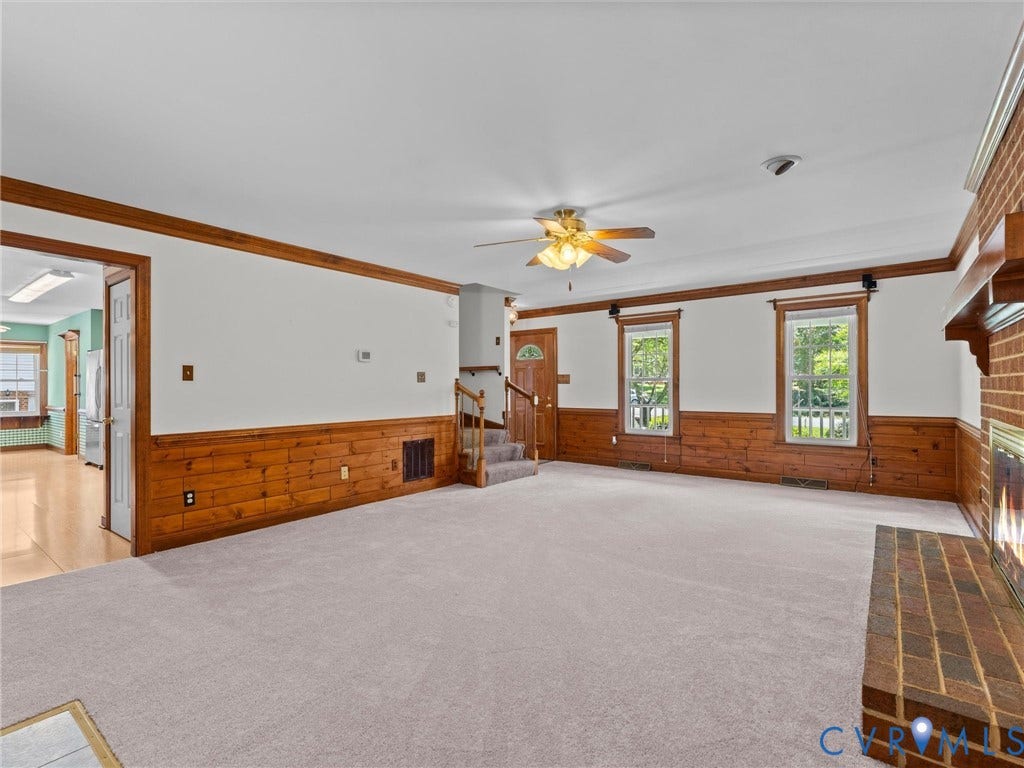 Spacious living area featuring light-toned carpeting and wood paneling accents