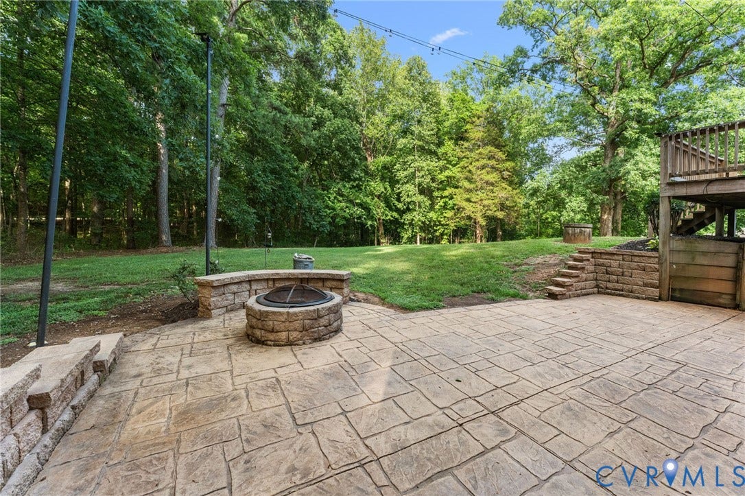1496 Dorset Road, Powhatan, Powhatan, VA 23139 Stamped concrete patio with a built-in stone fire pit, surrounded by a stone retaining wall and an expansive lawn