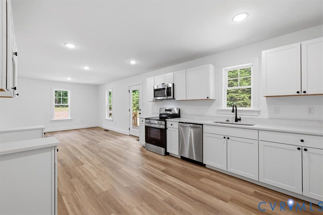 654 Frenchs Store Road, Cumberland, VA 23040 Open-concept kitchen and living area featuring wood-finish flooring, white cabinetry with black hardware, stainless steel appliances, and multiple windows