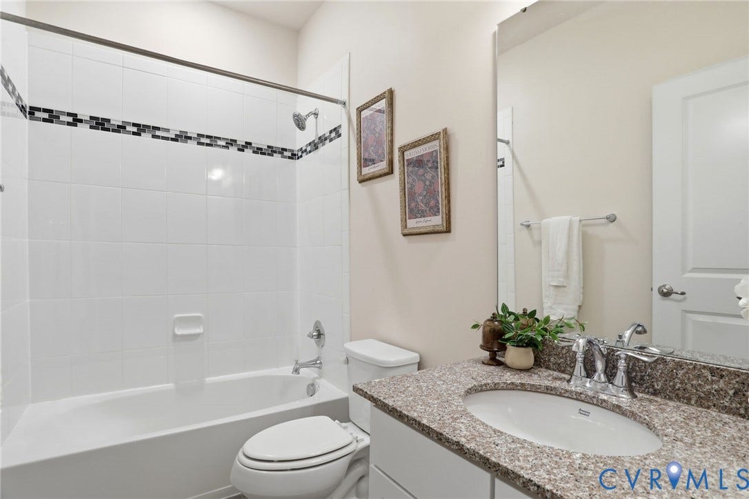 4101 New Hermitage Drive, Henrico, VA 23228 Bathroom featuring a white tub and shower combination with a decorative tile accent band, a built-in vanity with a granite-style countertop, an oval undermount sink, and chrome fixtures
