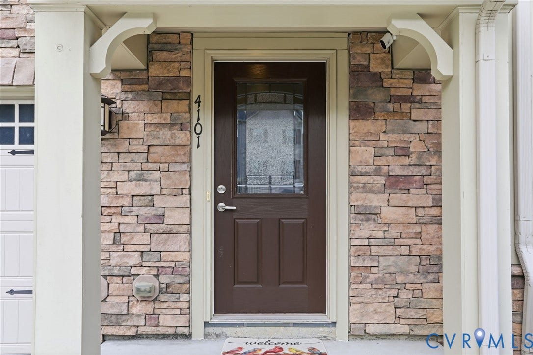 4101 New Hermitage Drive, Henrico, VA 23228 Entryway featuring a brown panel door with decorative glass, stone-finish siding, white trim, and a wall-mounted exterior light fixture