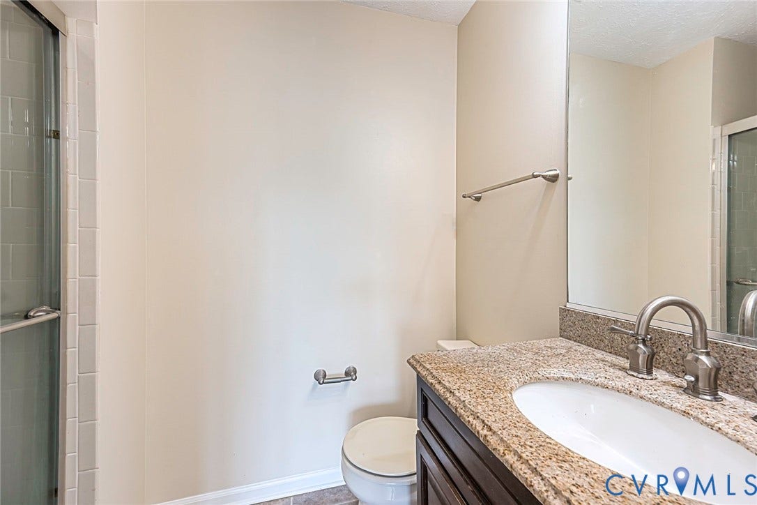 Bathroom featuring a granite countertop vanity with an undermount sink and brushed nickel faucet, a glass-enclosed shower, and neutral wall paint
