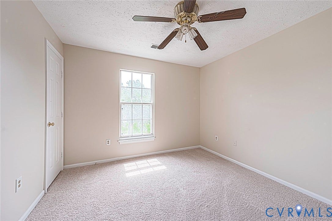 Neutral-toned room featuring a single window, light beige carpet, and a brass-finished ceiling fan with wood-finish blades