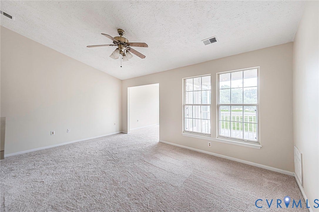 Carpeted living area featuring vaulted ceilings, a ceiling fan, and two large windows