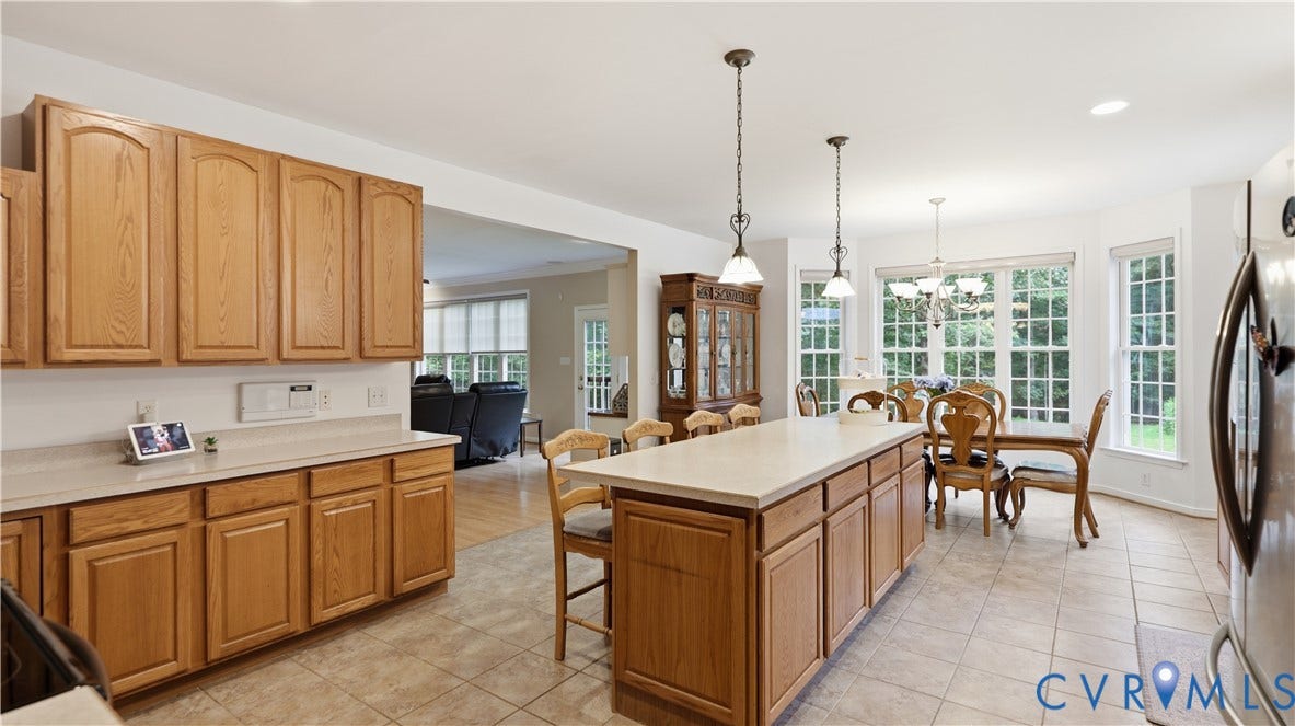 1836 Rocky Ford Road, Powhatan, VA 23139 Kitchen featuring ample cabinetry, a central island with bar seating, tile flooring, and a dining area with multiple large windows overlooking exterior greenery