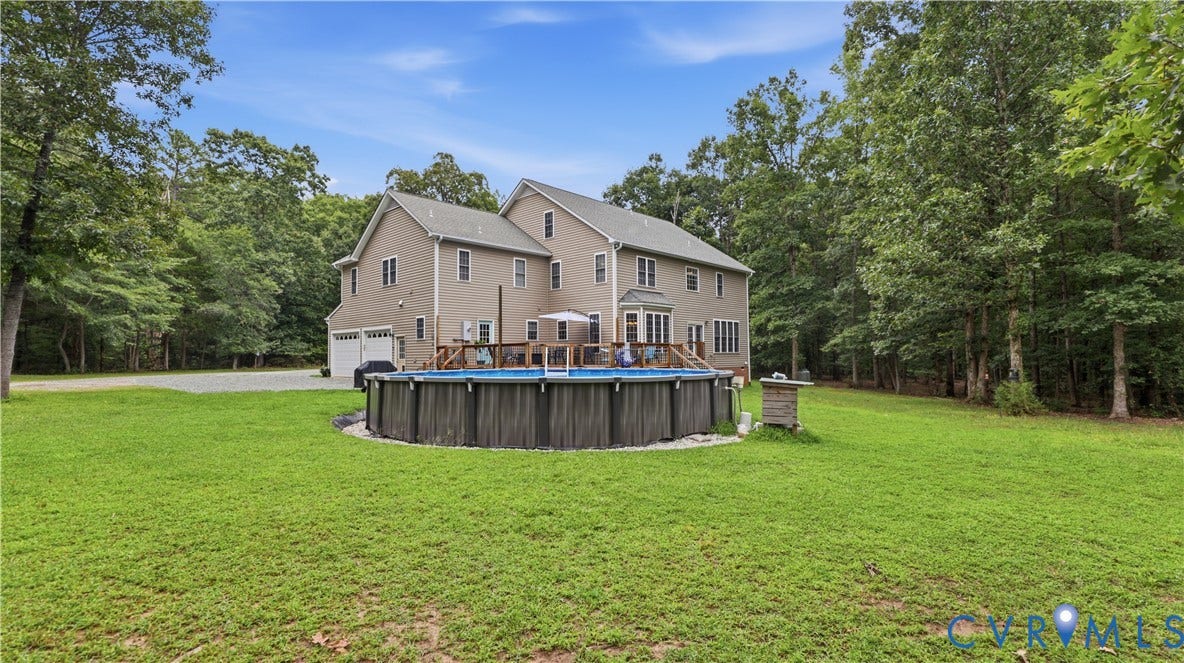 1836 Rocky Ford Road, Powhatan, VA 23139 Rear exterior featuring a custom deck with an above-ground pool, a spacious lawn, and a backdrop of mature trees