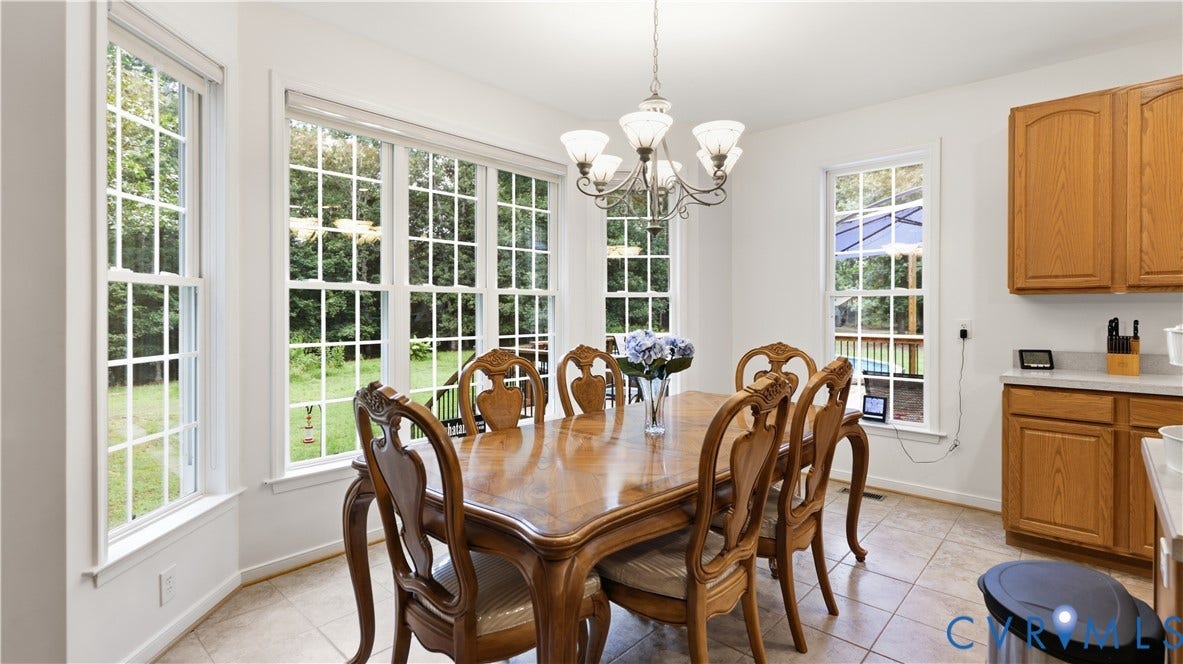 1836 Rocky Ford Road, Powhatan, VA 23139 Dining area featuring a bay window with grid-patterned glass, a multi-bulb chandelier, neutral-toned tile flooring, and wood-finish cabinetry