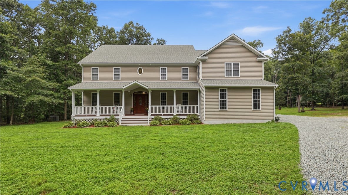 1836 Rocky Ford Road, Powhatan, VA 23139 Two-story residence featuring light beige siding, a deep red front door, a columned front porch with white railing, a gravel driveway, and a verdant lawn