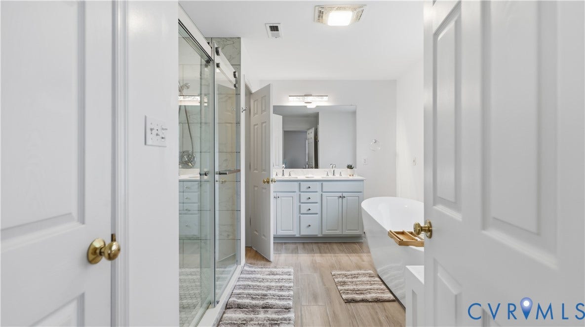 1836 Rocky Ford Road, Powhatan, VA 23139 Spacious bathroom featuring a frameless glass shower with tile surround, a freestanding soaking tub, a double vanity with white cabinetry, and wood-finish flooring