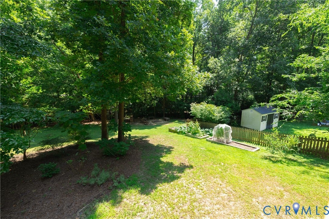 Expansive grassy yard featuring mature trees, raised garden beds, a storage shed, and a wood picket fence