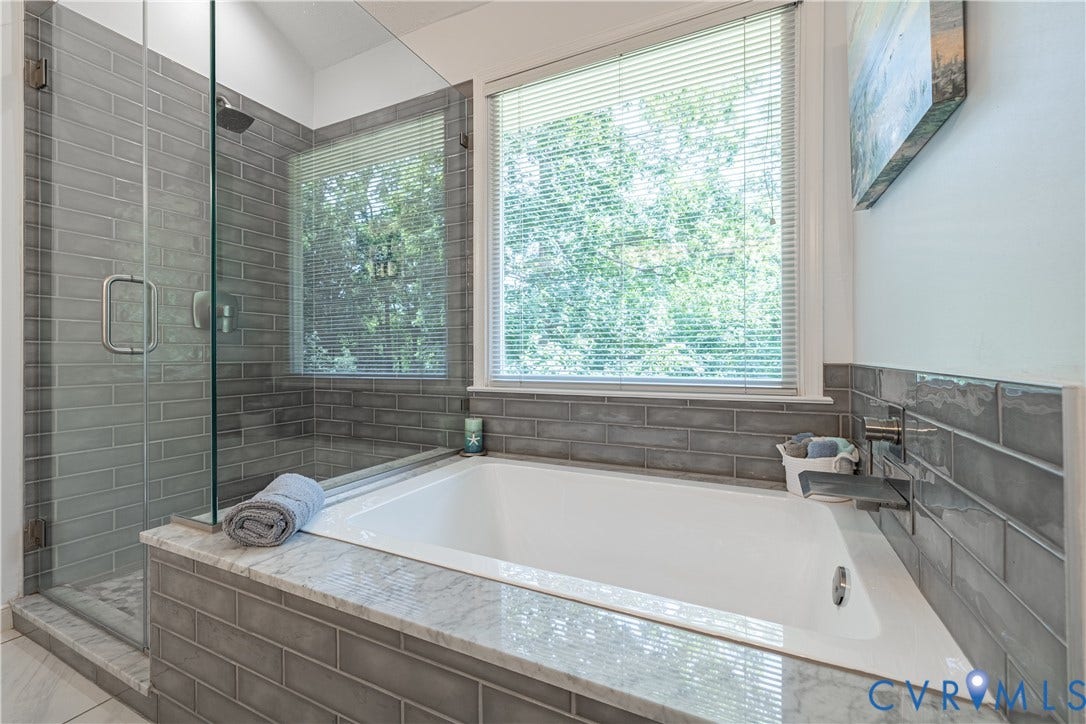 Built-in tub with stone-finish surround, accompanied by a glass-enclosed shower featuring subway tile