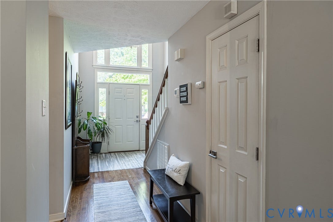 Two-story foyer featuring a paneled entry door with sidelights and transom window, a white painted staircase with wood handrail, and a mix of wood-finish and light-toned flooring