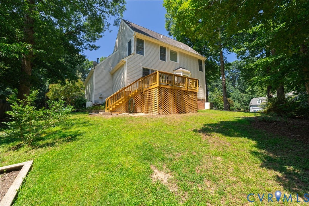 Rear exterior featuring a multi-level wood deck with lattice skirting and stairs descending to a grassy yard