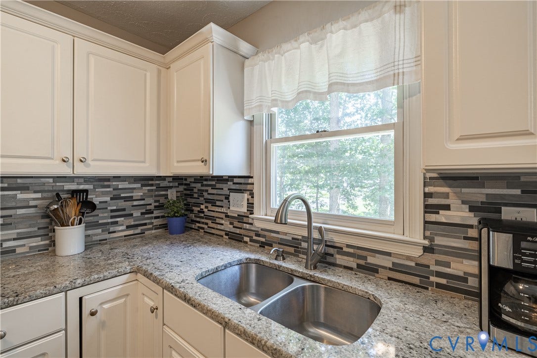 Kitchen featuring a double basin stainless steel sink with a gooseneck faucet, light-toned cabinetry, granite countertops, and a mosaic tile backsplash