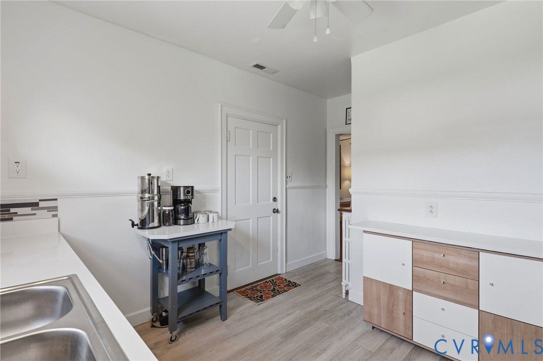 3332 Parkwood Avenue, Carytown, Richmond, VA 23221 Kitchen area featuring light wood-finish flooring, white walls with wainscoting, a double basin stainless steel sink, a multi-tone tile backsplash, and a contemporary storage console with white and wood-finish doors and drawers