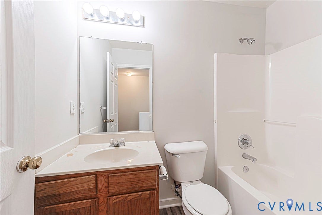 2802 Goyne Terrace, Chester, VA 23831 Bathroom featuring a wood-finish vanity with a built-in sink, a wall-mounted mirror, a four-light vanity fixture, a toilet, and a white bathtub with a shower