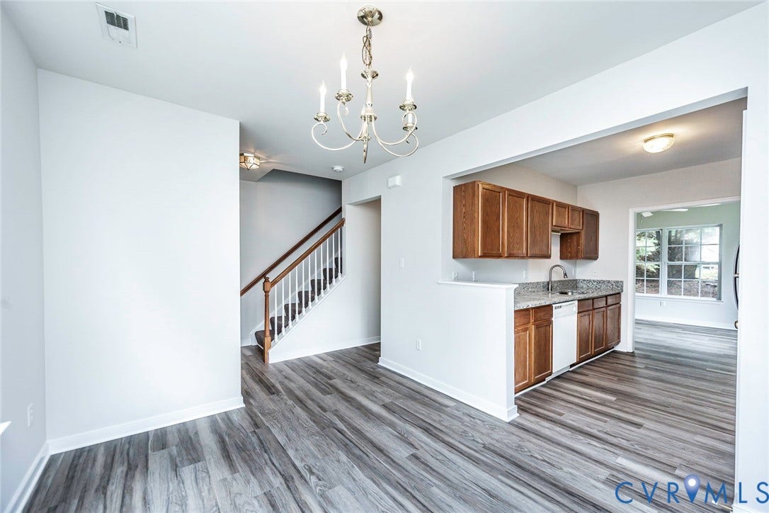 2802 Goyne Terrace, Chester, VA 23831 Open-concept living space featuring wood-finish flooring, a traditional chandelier, a staircase with wood handrails and white balusters, and a kitchen pass-through with wood cabinetry and a speckled countertop
