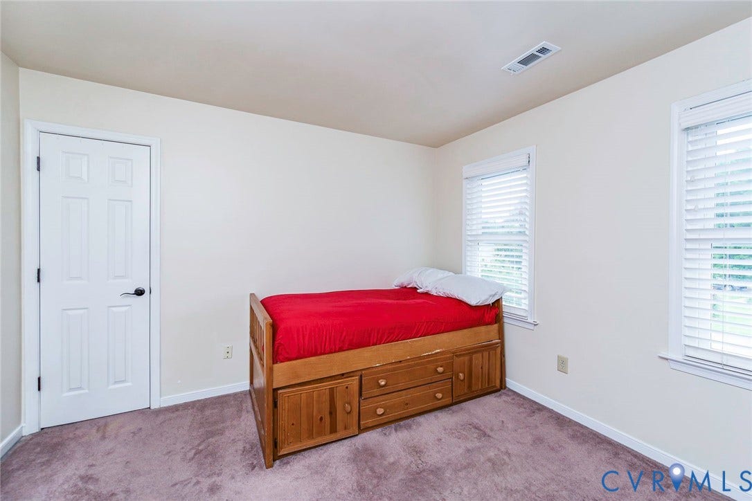 Room featuring two windows with horizontal blinds, carpeted flooring, and a white paneled door with black hardware