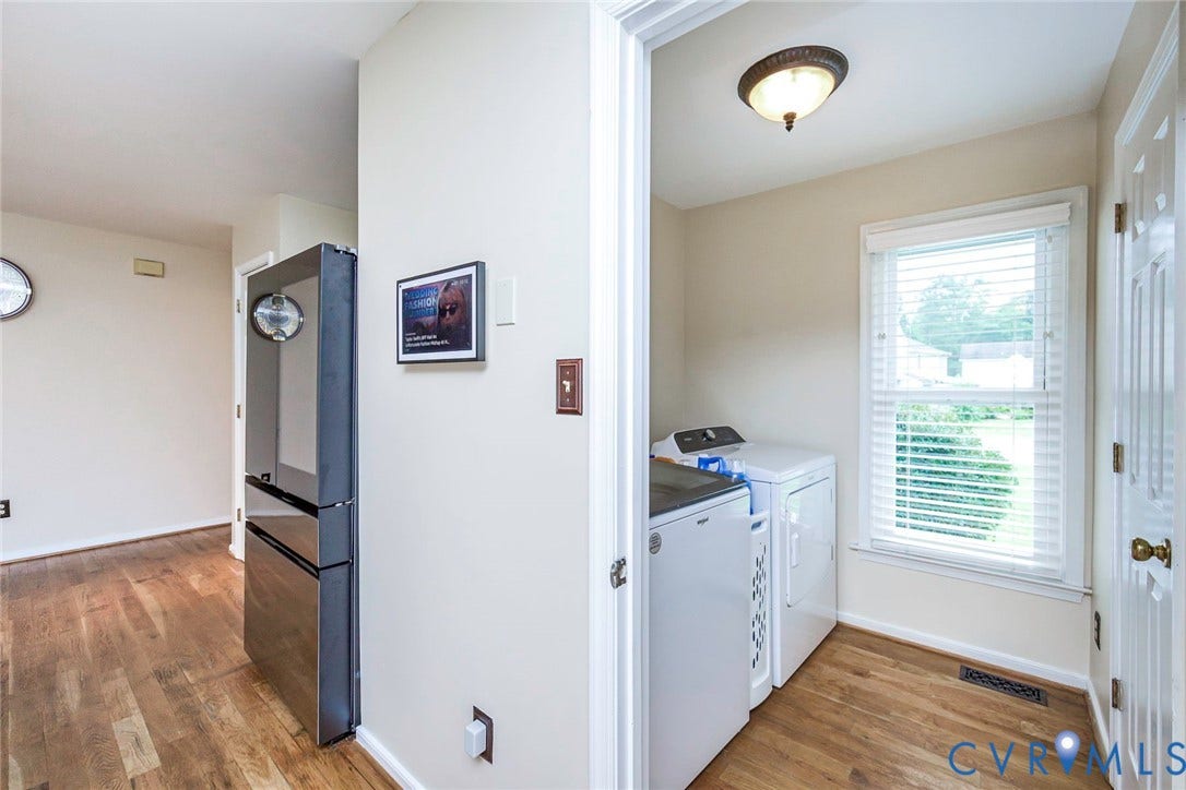 Dedicated laundry area featuring wood-finish flooring, a double window with blinds, and an overhead flush mount light fixture