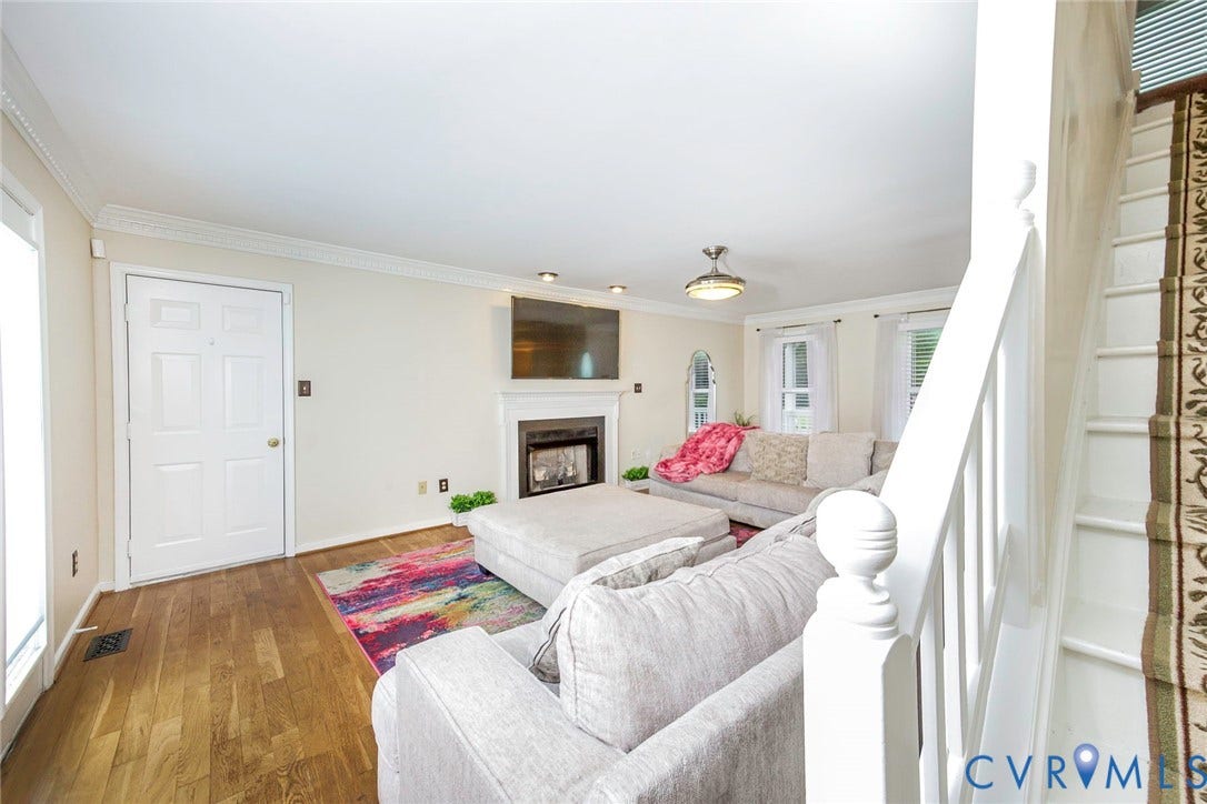Living area featuring wood-finish flooring, a white mantel fireplace, and crown molding