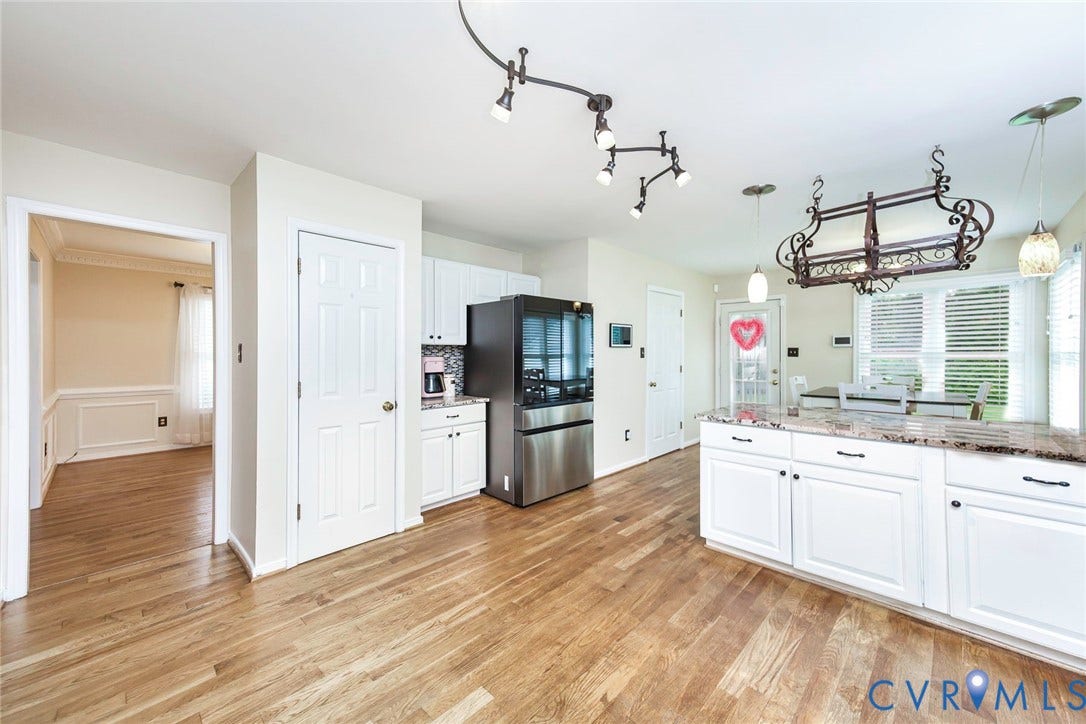 Kitchen featuring wood-finish flooring, white cabinetry with dark hardware, a center island with a stone countertop, a double-door stainless steel refrigerator, and recessed lighting