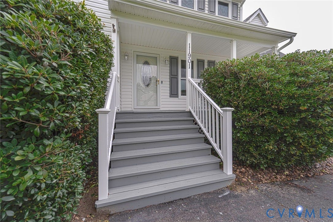 Inviting front entrance featuring a covered porch, white vinyl siding, and grey painted steps with white railings
