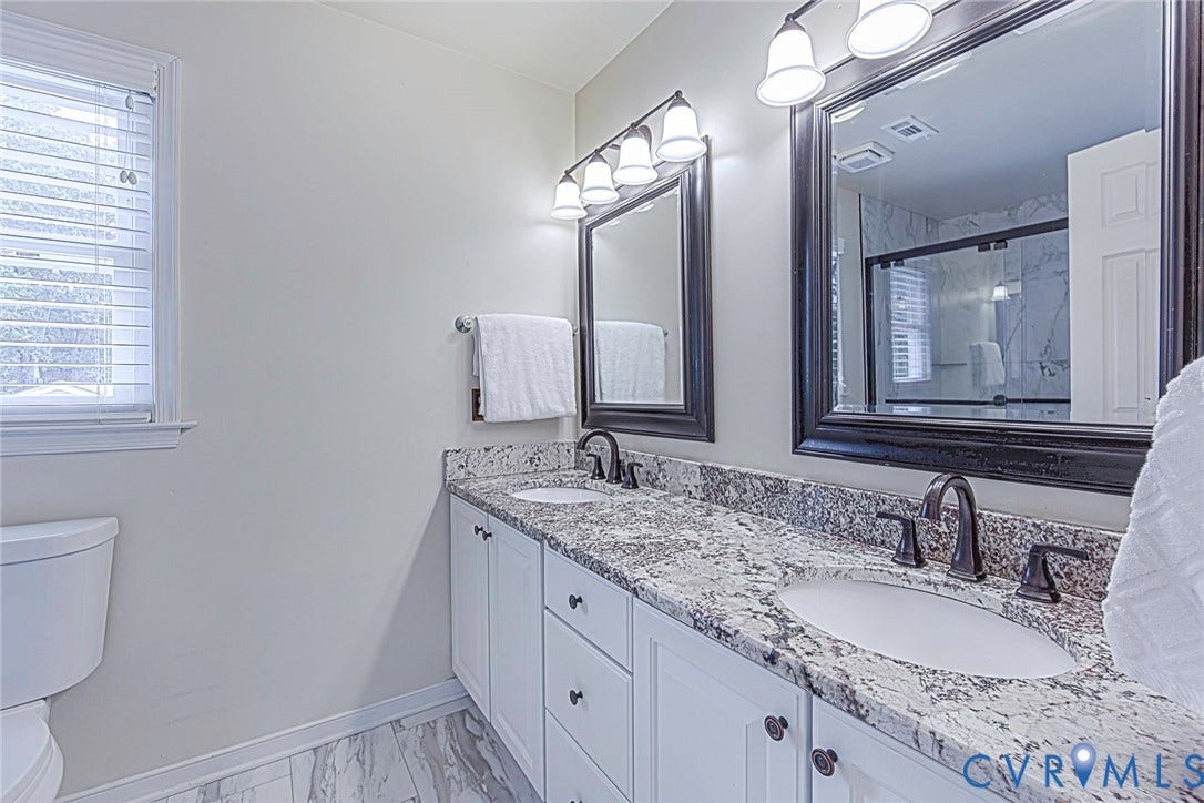 Double vanity featuring white cabinetry, granite countertops, and two undermount sinks with oil-rubbed bronze fixtures