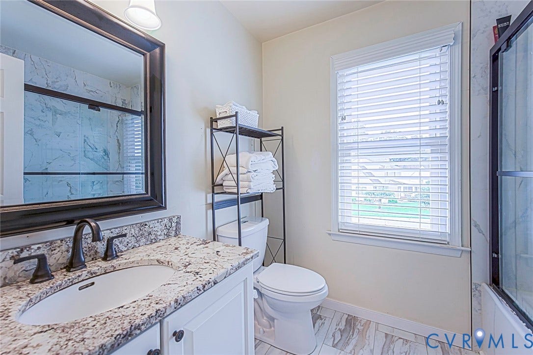 Bathroom vanity featuring a light granite countertop with an undermount sink, dark bronze fixtures, and a framed mirror