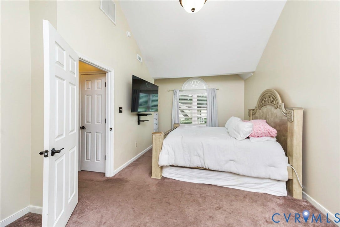 Vaulted ceiling bedroom featuring plush carpeting, a multi-pane window with arched transom, and a ceiling-mounted light fixture