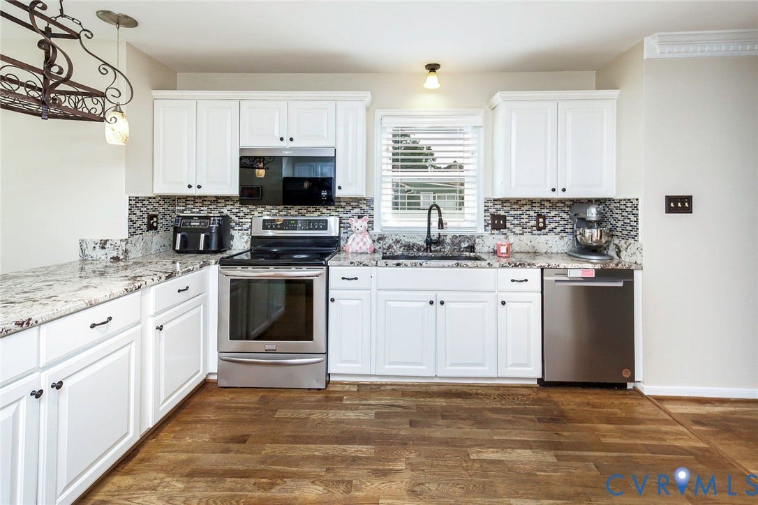 Kitchen featuring white cabinetry, light-toned countertops, a mosaic tile backsplash, stainless steel appliances, and wood-finish flooring