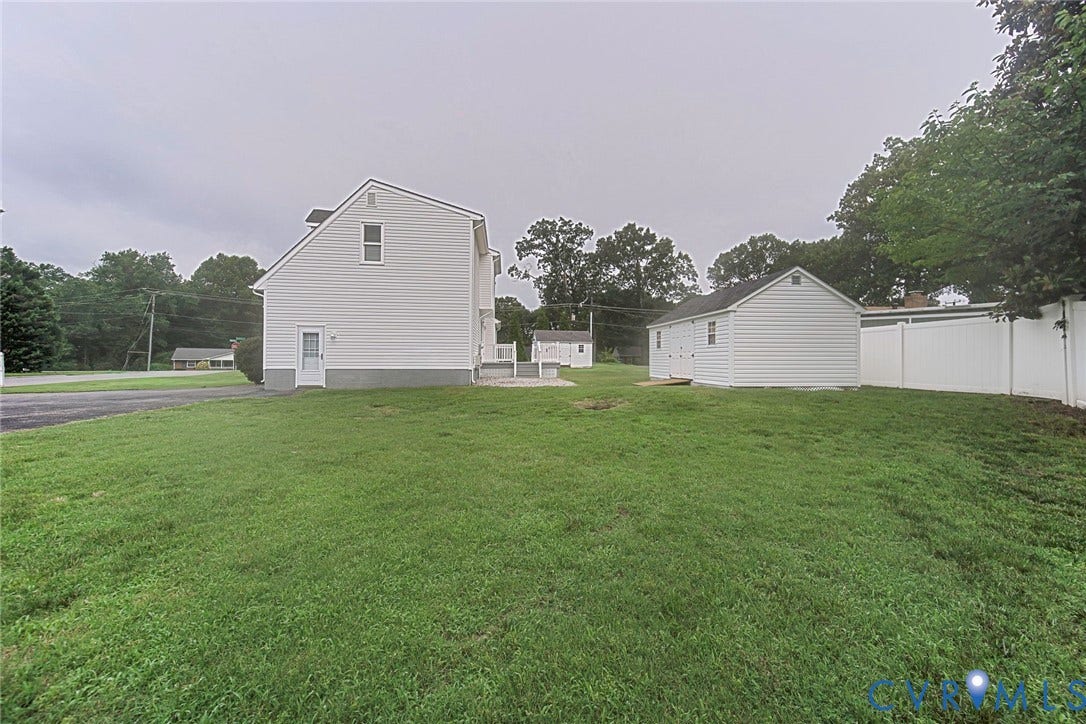 Expansive green lawn with a white vinyl fence and a detached white storage building